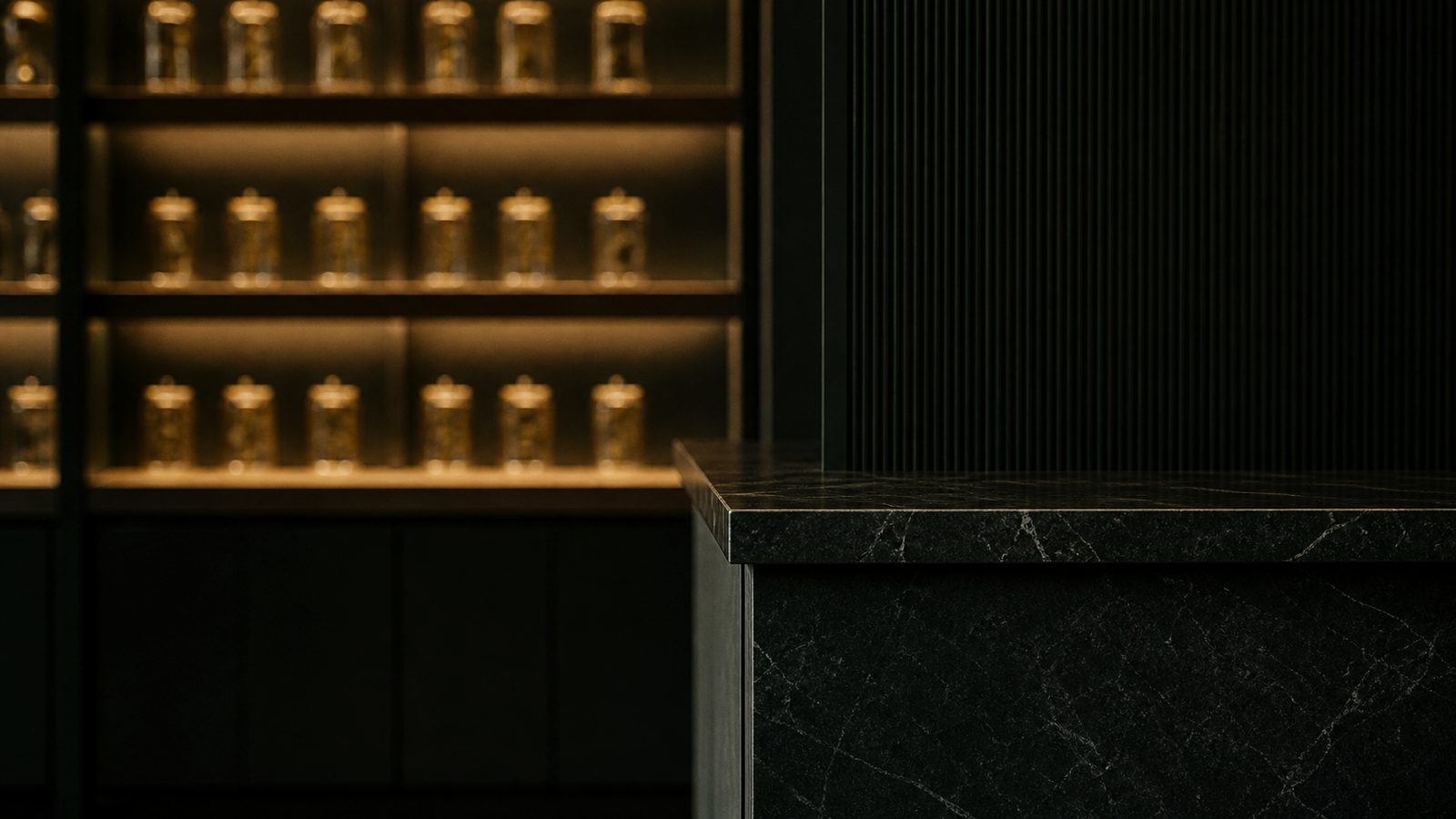 Dark stone counter beside softly lit shelving of amber jars